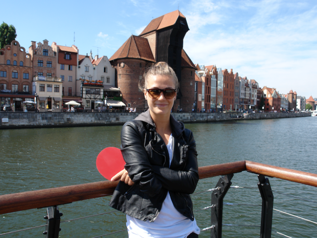 Natalia Partyka w okularach przeciwsłonecznych stoi z założonymi rękami trzymając paletkę w tle nabrzeże w Gdańsku