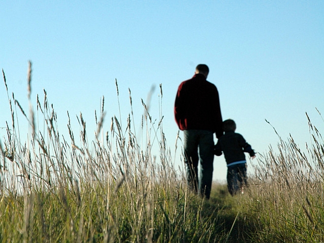 Widziani z tyłu ojciec z małym synem podczas spaceru wśród traw