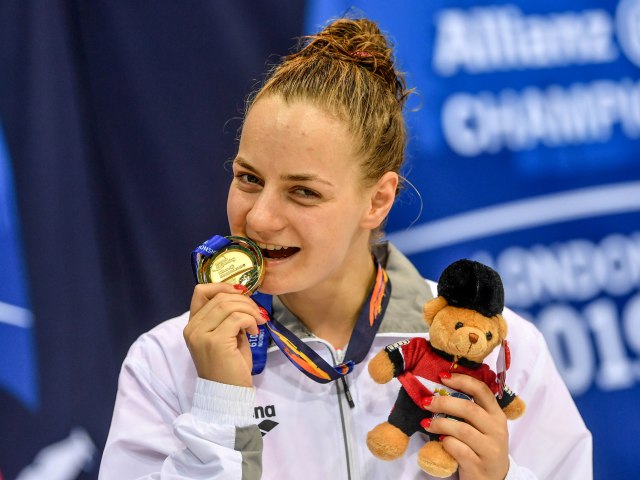 Oliwia Jabłońska uśmiechnięta trzyma medal w zębach w drugiej ręce misia