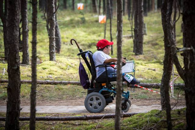 mężczyzna na wózku podczas zawodów z orientacji precyzyjnej w lesie pośród drzew