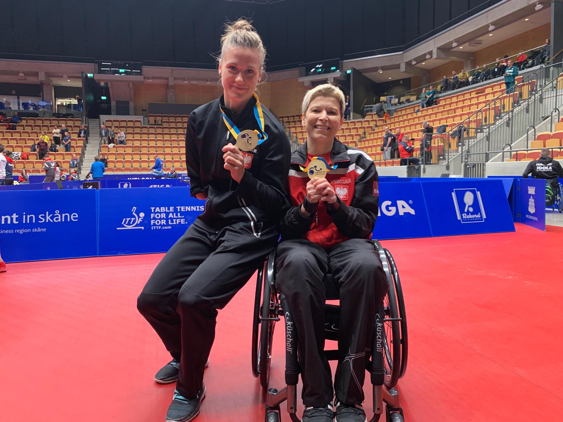 Natalia Partyka siedzi bokiem na wózku Doroty Bucław obie uśmiechnięte pokazują medale