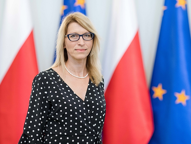 Paulina Malinowska-Kowalczyk stoi na tle flag Polski i Unii Europejskiej