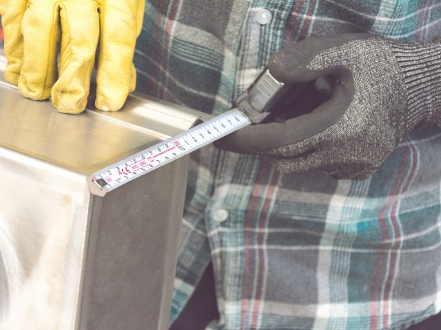 mężczyzna w rękawicach roboczych wykonuje pracę fizyczną, mierzy metrem aluminiowy przedmiot