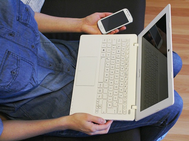 dziewczyna siedząc trzyma na kolanach laptopa i komórkę w lewej ręce