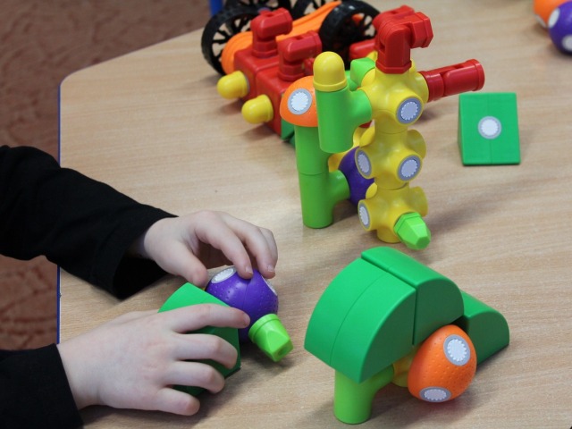 ręce chłopca na stole układają klocki stoją inne kolorowe części zabawek na stole