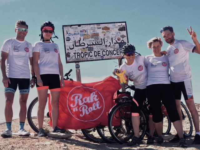 5 osób przy znaku zwrotnik raka rowerami i flagą z napisem rak n roll