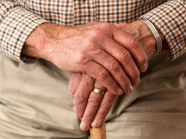 dłonie seniora oparte o drewnianą laskę