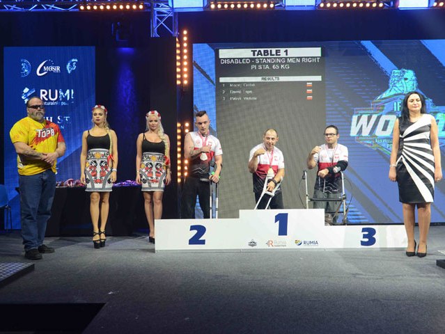 na podium zawodnicy z niepełnosprawnością na pierwszym miejscu stoi Maciej Gralak z podniesoną w geście zwycięstwa ręką