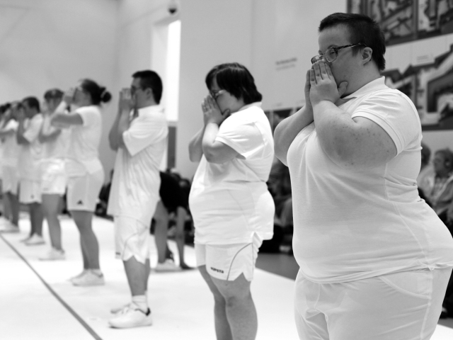 aktorzy z zespołem downa w strojach sportowych stoją w rzędzie i trzymają ręce przy twarzy, zdjęcie czarno-białe