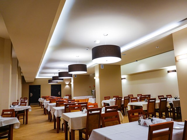 sala jadalna z czterosobowymi miejscami przy stołach z bialym obrusem i krzesłami