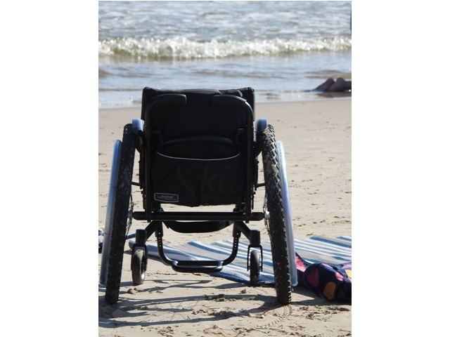 pusty wózek stoi na plaży przed nim widać morze obok rozłożona mata na piasku