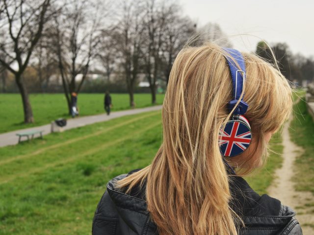 młoda dziewczyna odwrócona tyłem w parku ze słuchawkami na uszach na których jest rysunek angielskiej flagi