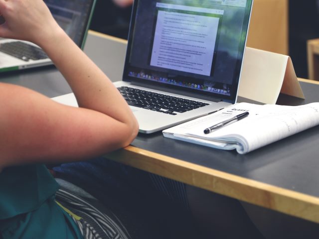 młoda kobieta siedzi przed laptopem widać tylko jej rękę opartą o biurko