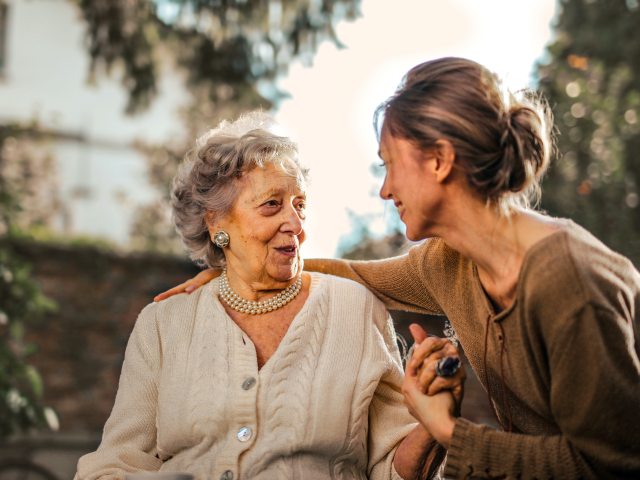 młoda kobieta uśmiechnięta trzyma za rekę starszą kobietę w bliskim kontakcie