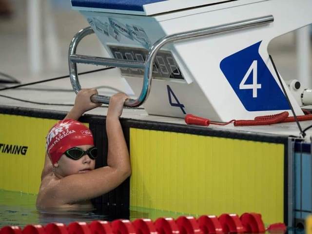 Filip Matusiak w basenie w czepku i okularach pływackich trzyma się przy miejscu startowym
