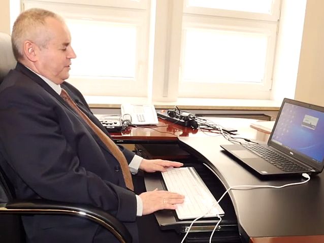Minister Paweł Wdówik siedzi przy biurku przed laptopem, trzymając ręce na klawiaturze