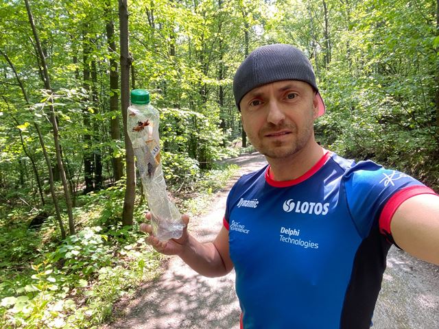Kajetan_Kajetanowicz w sportowym stroju w lesie trzyma w ręku zużytą plastikową butelkę