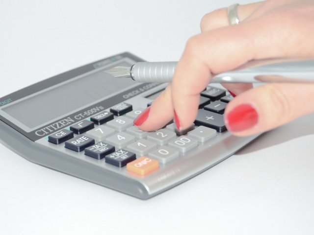 kobieca ręka trzyma pióro wieczne i palcami wciska przyciski kalkulatora