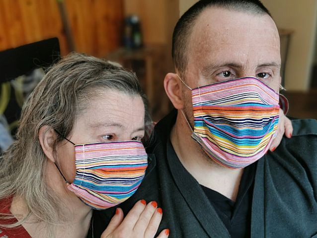 Kobieta i mężczyzna - obydwoje to osoby z zespołem Downa - siedzą przytuleni w maseczkach na twarzach