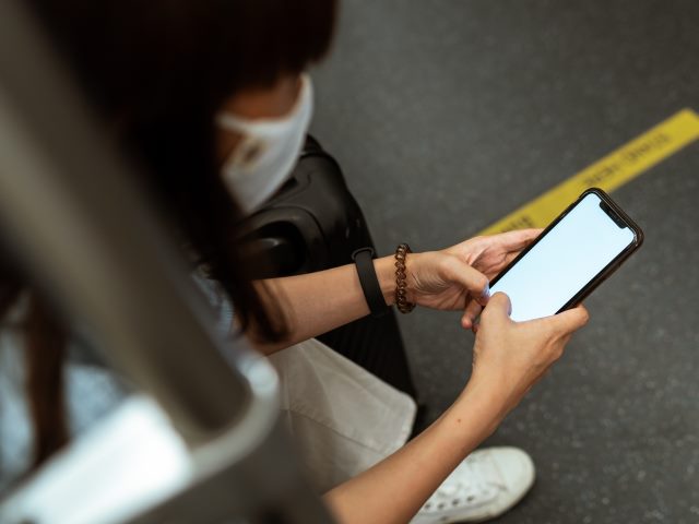 kobieta w maseczce siedzi w metrze z telefonem w ręce widać na podłodze żółtą linię