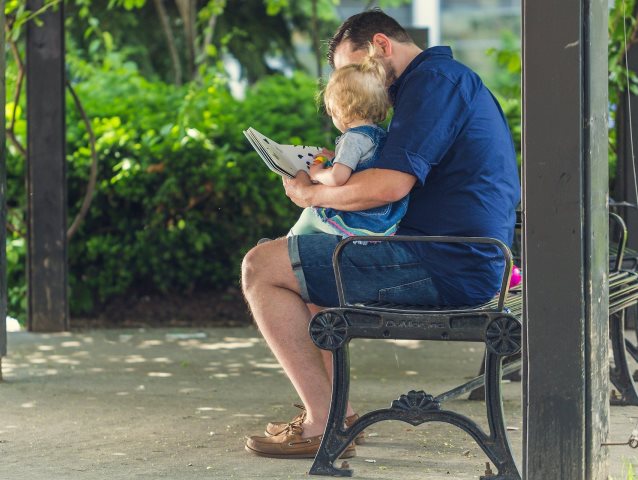 na krześle na tarasie siedzi ojciec z małym dzieckiem na kolanach i oglądają książkę