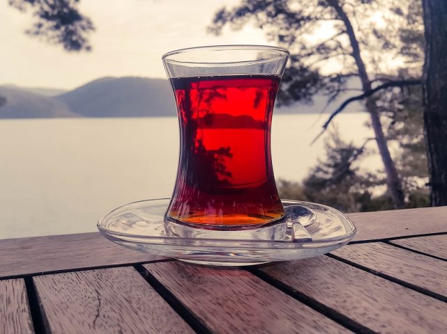 szklanka z herbatą na spodku stoi na drewnianym stole w tle jezioro i pagórki