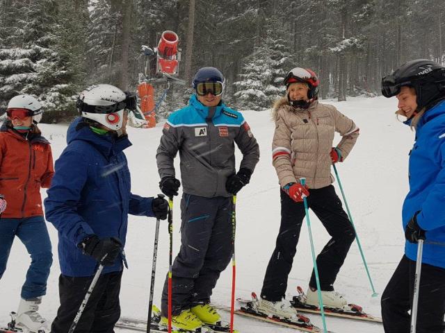 3 kobiety i dwóch mężczyzna stoją na stoku na nartach