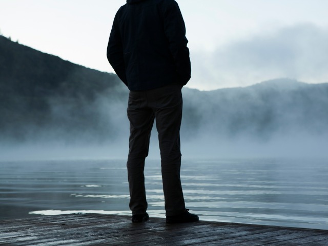 samotny męzczyzna widoczny od tyłu, nie widać głowy stoi nad jeziorem