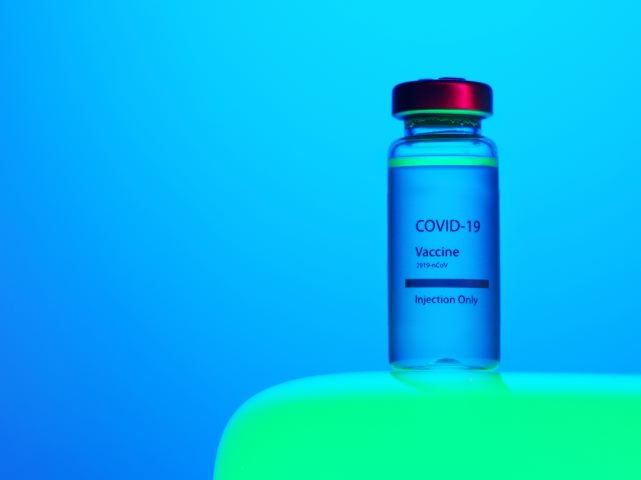 na niebieskim tle stoi buteleczka z napisem covid-19 vaccine na zielonym przedmiocie