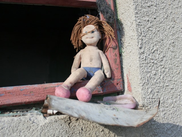 w starej odrapanej ramie okiennej bez szyby siedzi szmaciana brudna lalka