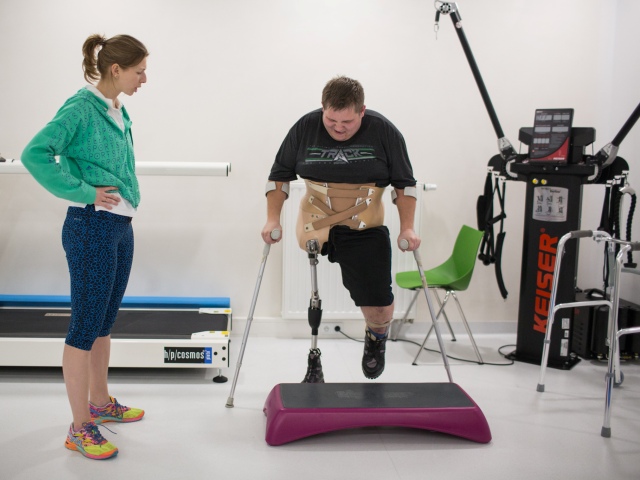 mężczyzna z protezą jednej nogi podczas ćwiczeń na sali obok niego fizjoterapeutka