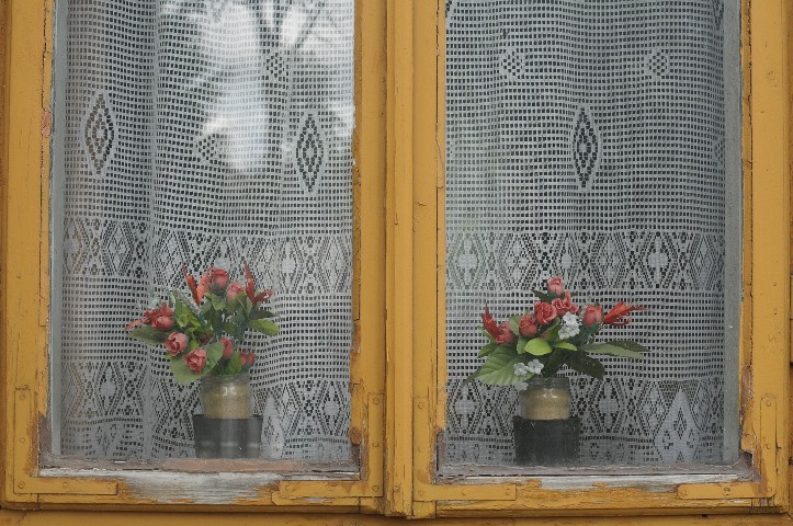 stare odrapane okno z z pożółkłymi firankami i sztucznymi bukietami w słoikach