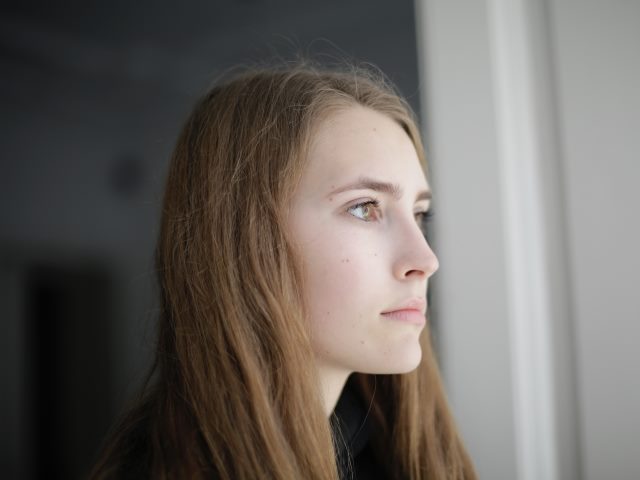 młoda kobieta z długimi włosami z poważną miną patrzy przez okno