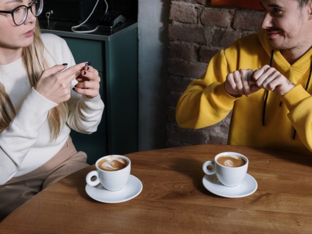 kobieta i mężczyzna w kawiarni migają siedząc przy stoliku na którym stoją dwie filiżanki kawy