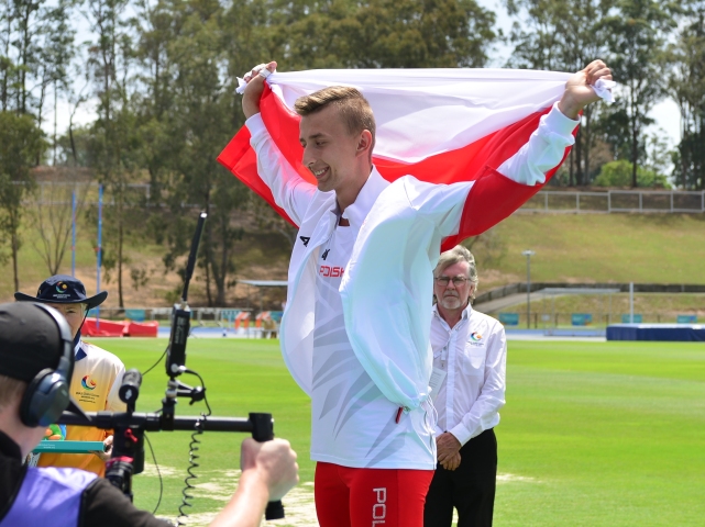 uśmiechnięty zawodnik z uniesioną nad głową polsko-czerwoną flagą