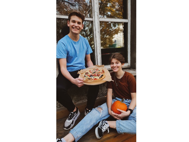 chłopak trzyma pizzę a dziewczyna siedzi na ziemi i trzyma dynię pozując z uśmiechami
