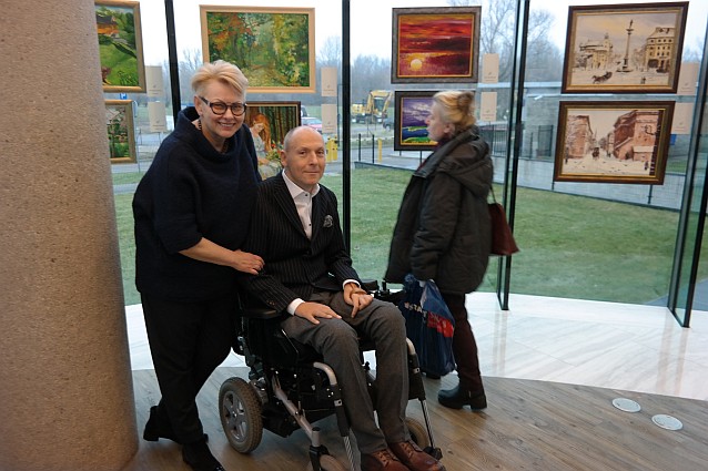 Ewa Pawłowska i Piotr Pawłowski pozują do zdjęcia na tle wiszących za nimi obrazów