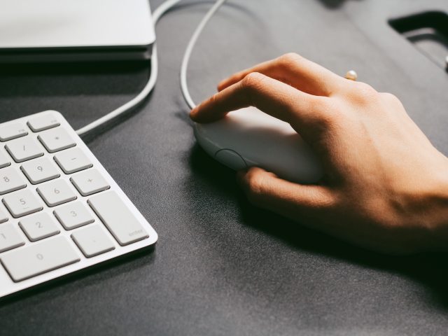 dłoń na myszy komputerowej, obok klawiatura