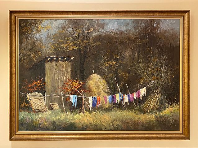 Wiszący na ścianie obraz przedstawia kolorowe pranie rozwieszone na wsi pod lasem, przy wygódce i stogu siana