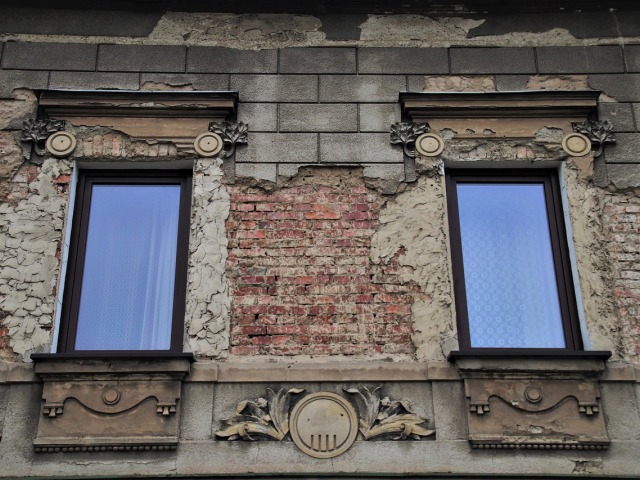 Dwa okna w zniszczonym budynku, z opadającym tynkiem.