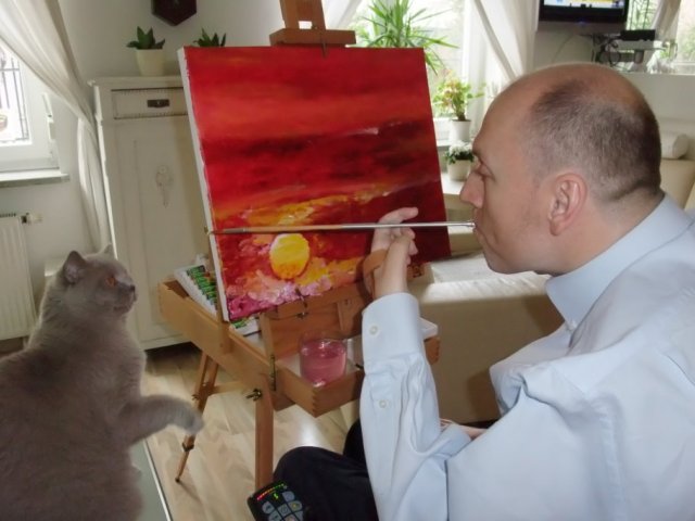 Piotr pawłowski maluje obraz ustami w pokoju obok siedzi kot