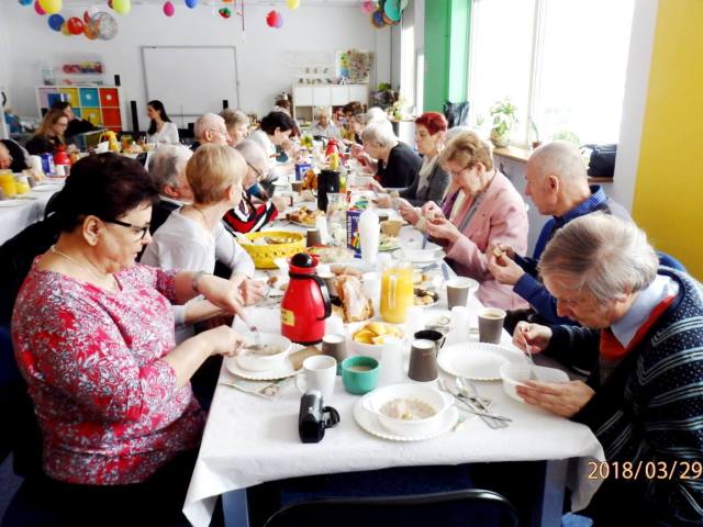 seniorzy w Centrum Wielu Pokoleń w Bydgoszczy siedzą przy zastawionych stołach i jedzą