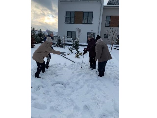 trzy seniorki zimą na śniegu przed domem opieki wraz z młodszą dziewczyną roześmiane