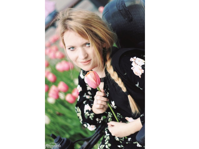 sylwia błach siedzi na wózku trzymając w ręku tulipana uśmiecha się do obiektywu