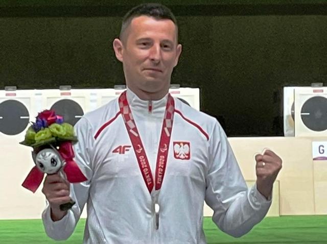 uśmiechnięty Szymon Sowiński stoi na podium. Na szyi ma srebrny medal, w dłoni maskotkę mistrzostw