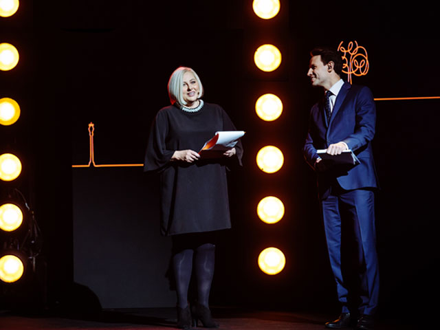 Na scenie od lewej Ewa Pawłowska i Tomasz Wolny. Są elegancko ubrani. Wokół jest dość ciemno, scenę oświetla rząd okrągłych pionowych lampek za prezenterami