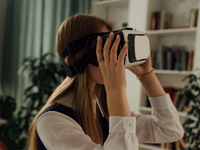 dziewczyna ma na oczach google z wirtualnej rzeczywistości, trzyma je delikatnie dłońmi. jest w pokoju