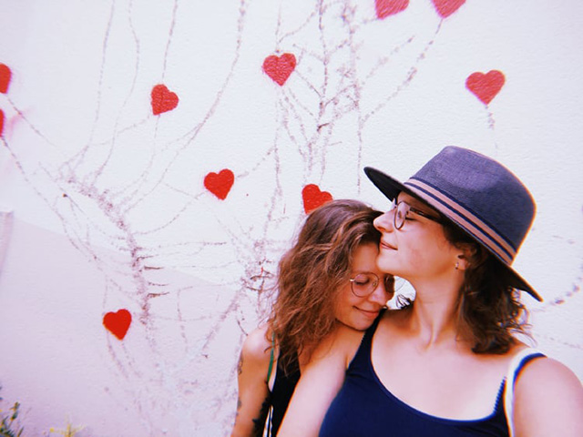 Zuzanna i jej partnerka Justyna przytulają się na tle ściany ozdobionej serduszkami.