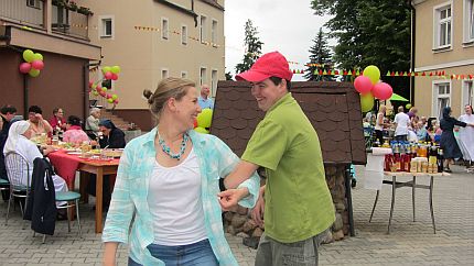 Uśmiechnięta kobieta tańczy z roześmianym młodym mężczyzną na dziedzińcu budynku podczas pikniku