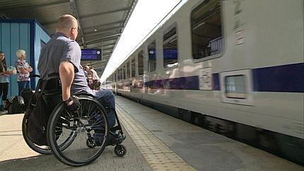 Mężczyzna na wózku na peronie dworca. Przed nim - wagon pociągu
